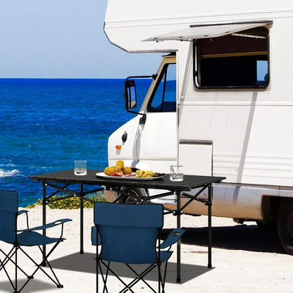 Klappbarer schwarzer Campingtisch aus Aluminium vor einem Wohnmobil am Meer, mit Campingstühlen und gedeckter Tischplatte